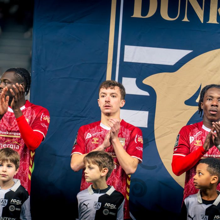 Trois joueurs de l’USL Dunkerque applaudissent devant la banniere du club